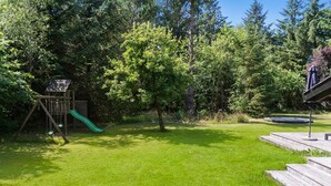 A backyard with a wooden play structure, a green slide, and a trampoline.
