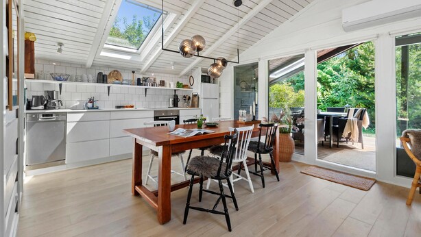 A modern kitchen with white cabinetry, a wooden dining table, and a large skylight.