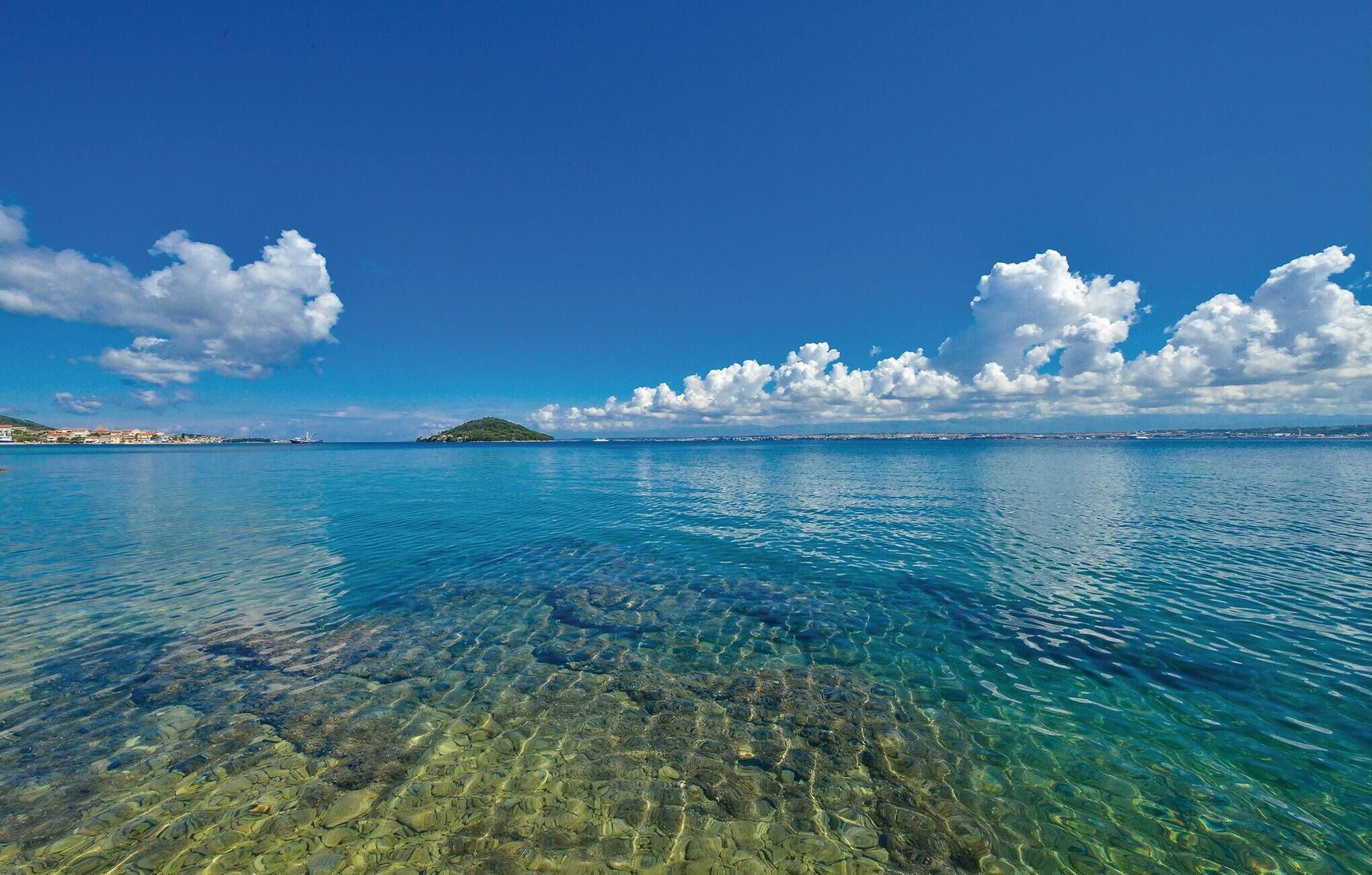 A clear view of a coastal area with calm waters, a distant island, and a clear sky.