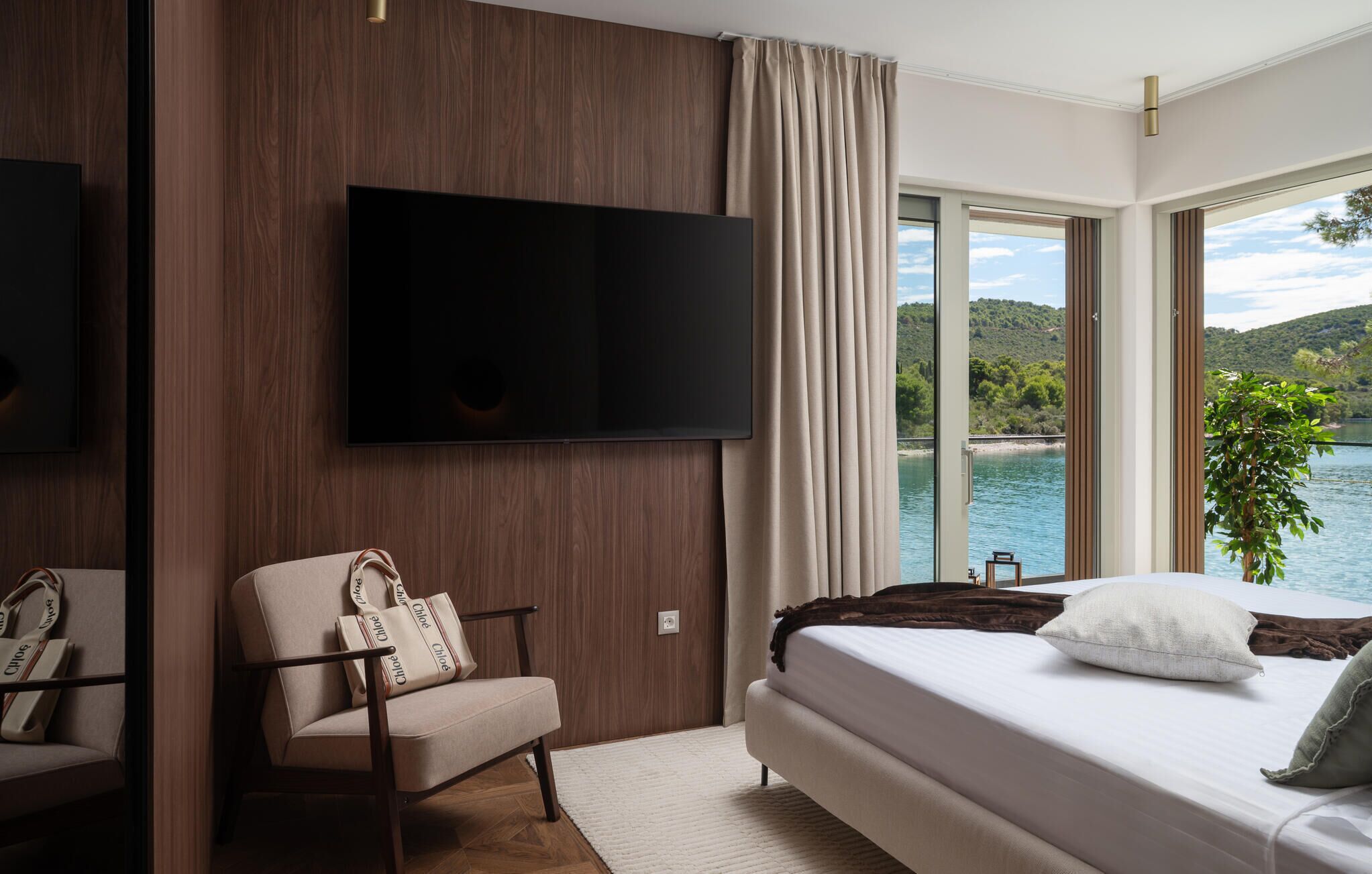 A hotel room with a bed, a chair, a TV, and a view of a lake.