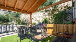 A covered patio with outdoor furniture, a stone wall, and a wooden fence. - Nice apartment in Omis with WiFi (Omis)