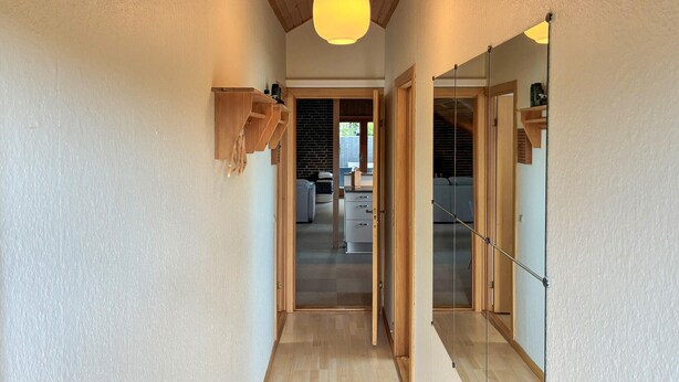 Un couloir avec des armoires en bois, un luminaire au plafond et une vue sur une pièce où se trouvent un lit et un bureau.