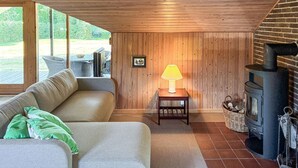 Un salon chaleureux avec un canapé, une table avec une lampe, une cheminée et une vue sur l’extérieur.