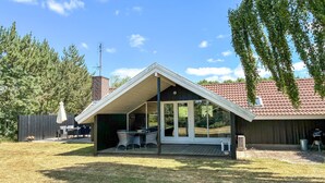 Un espace extérieur aménagé, abrité, avec une table et des chaises, un barbecue et une vue sur une maison dont le toit est recouvert de tuiles rouges.