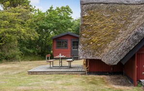 A rustic cabin with a thatched roof, a small wooden deck with a table and benches, and a red exterior. - Gorgeous home in Rømø with WiFi (Rømø)