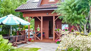 Une maison en bois avec un toit en tuiles, une véranda avec des chaises et des plantes en pot.