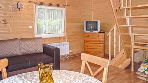 L’intérieur d’un chalet en bois, avec un canapé, une table, un téléviseur et une fenêtre avec des rideaux.