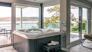 Um banheiro moderno com hidromassagem, janelas amplas e vista para um lago.