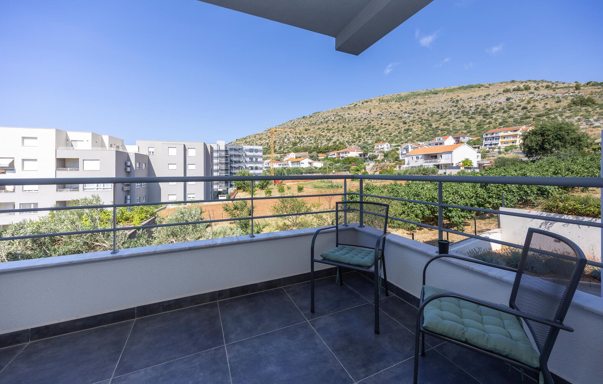 Ein Balkon mit zwei Stühlen und Blick auf eine Hügellandschaft mit Gebäuden unter blauem Himmel.