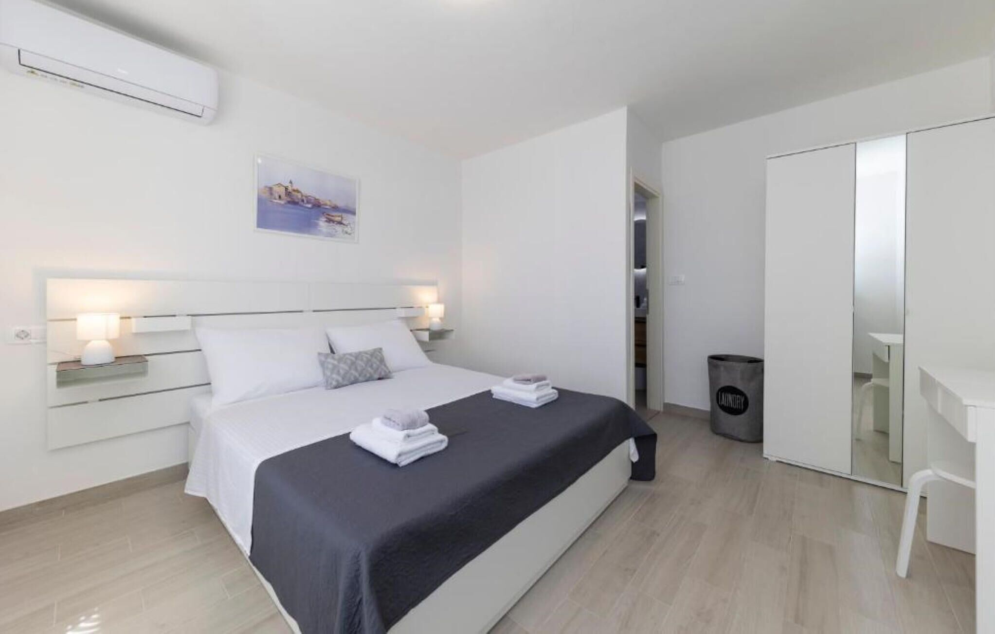 A modern hotel room with a neatly made bed, bedside lamps, a painting on the wall, and a wardrobe.