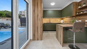 Una cocina moderna con detalles de madera, un lavamanos empotrado y vista a una piscina exterior.