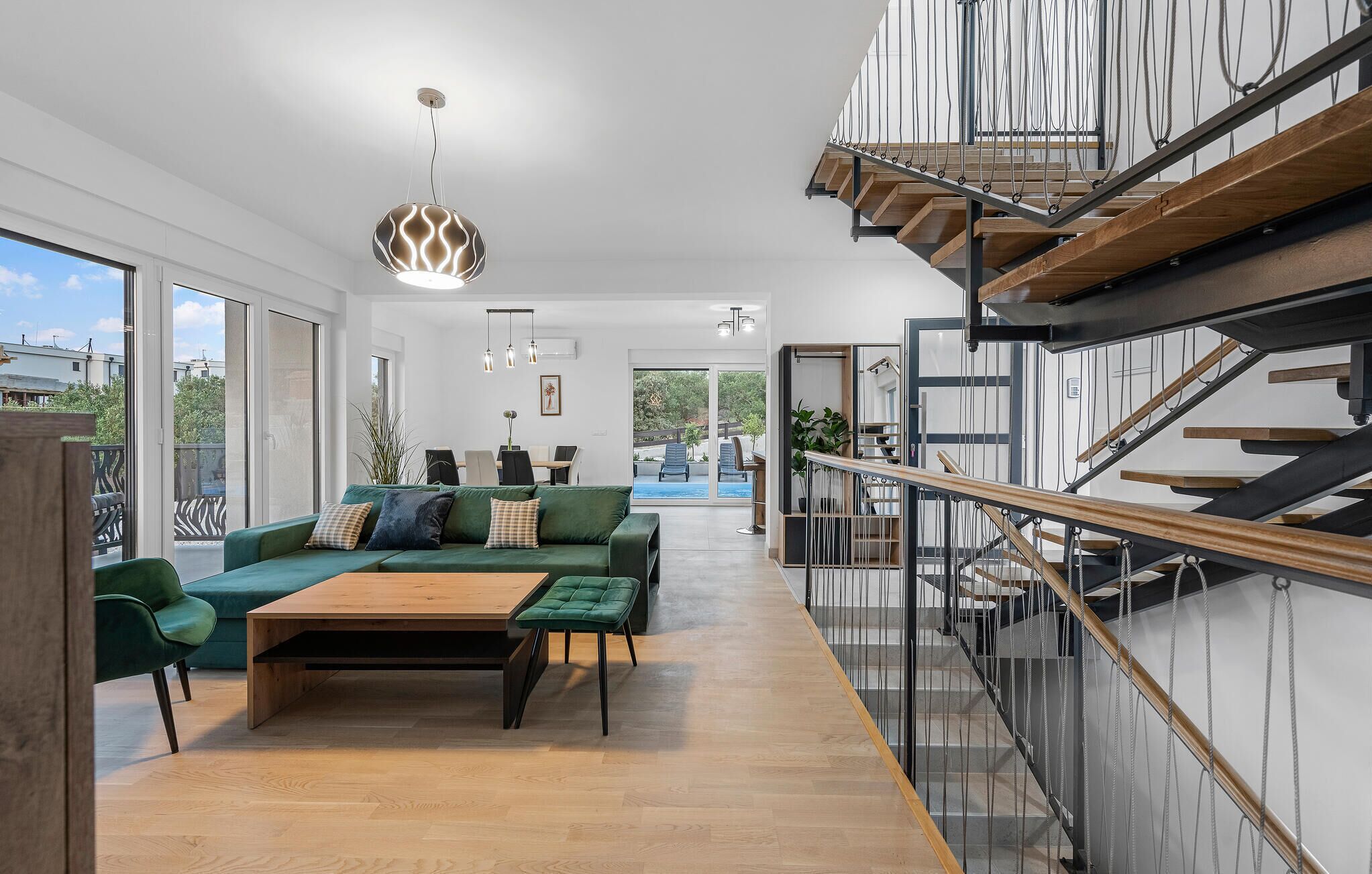 A modern living room with a green sofa, wooden coffee table, and a staircase with a glass railing.