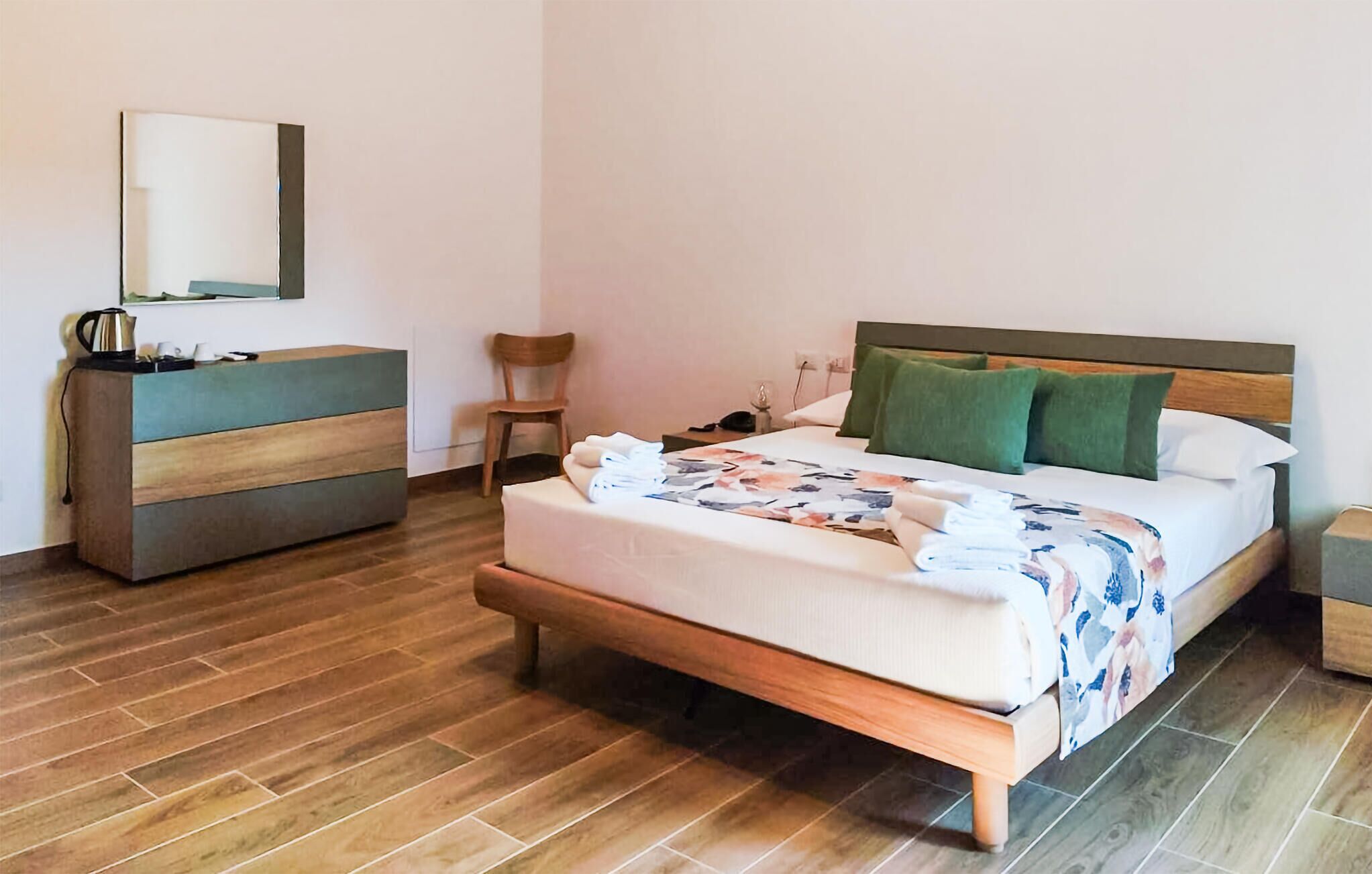 A hotel room with a bed, a bedside table, a chair, a dresser, and a mirror.