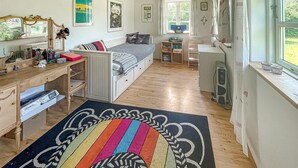 Habitación compacta y bien iluminada con cama, escritorio y pequeña kitchenette. Hay cuadros en las paredes y una ventana con cortinas.