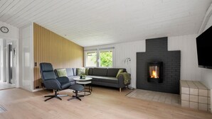 Un salon moderne comprenant un canapé, deux fauteuils, une petite table, une cheminée et un téléviseur fixé au mur.