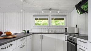 Une cuisine moderne avec des meubles blancs, un plan de travail noir, un four à micro-ondes, un four traditionnel et une fenêtre donnant sur un paysage verdoyant.