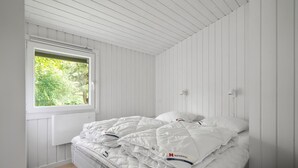 Une chambre à coucher avec un lit, du linge de lit blanc, une fenêtre donnant sur un paysage verdoyant et des murs blancs.