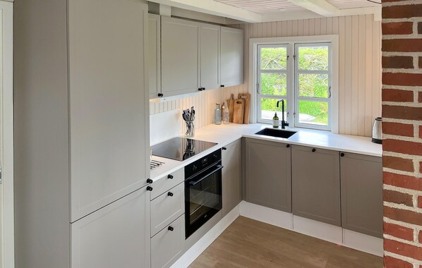 A kitchen with white cabinets, a black oven, a window with a view of greenery, and a brick wall.