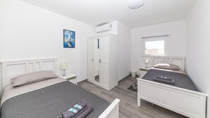 A hotel room with two single beds, a wardrobe, an air conditioning unit, a bedside table with a lamp, and a window with a view. - 2 bedroom lovely apartment in Stanici (Stanici)