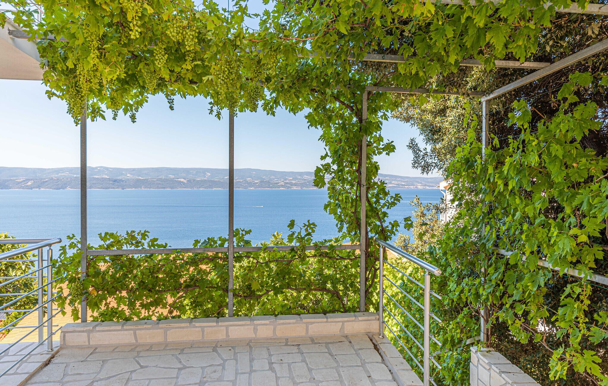 A stone-paved balcony with a metal railing overlooking a sea view.