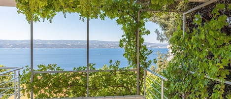 A stone-paved balcony with a metal railing overlooking a sea view.