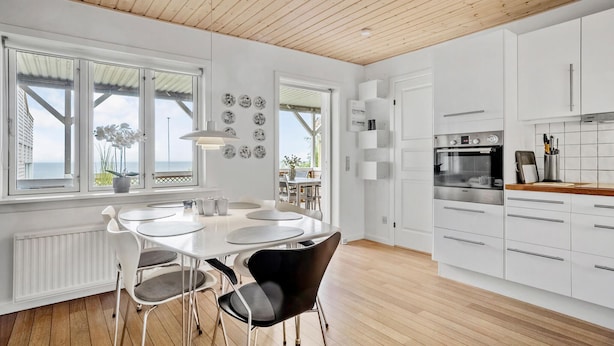 A modern kitchen with white cabinets, a built-in oven, and a dining area with a table and chairs. - 3 bedroom beautiful apartment in Allinge (Allinge)