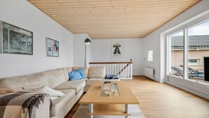 A living room with a wooden ceiling, a beige sofa, a coffee table, and a large window with a view of the outside. - 3 bedroom beautiful apartment in Allinge (Allinge)