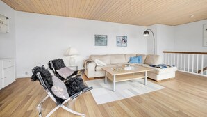 A modern living room with a wooden ceiling, a sofa, a coffee table, and a chair with a fur throw. - 3 bedroom beautiful apartment in Allinge (Allinge)
