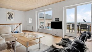 A spacious living room with a wooden ceiling, a large TV, and a view of the sea through the sliding glass doors. - 3 bedroom beautiful apartment in Allinge (Allinge)