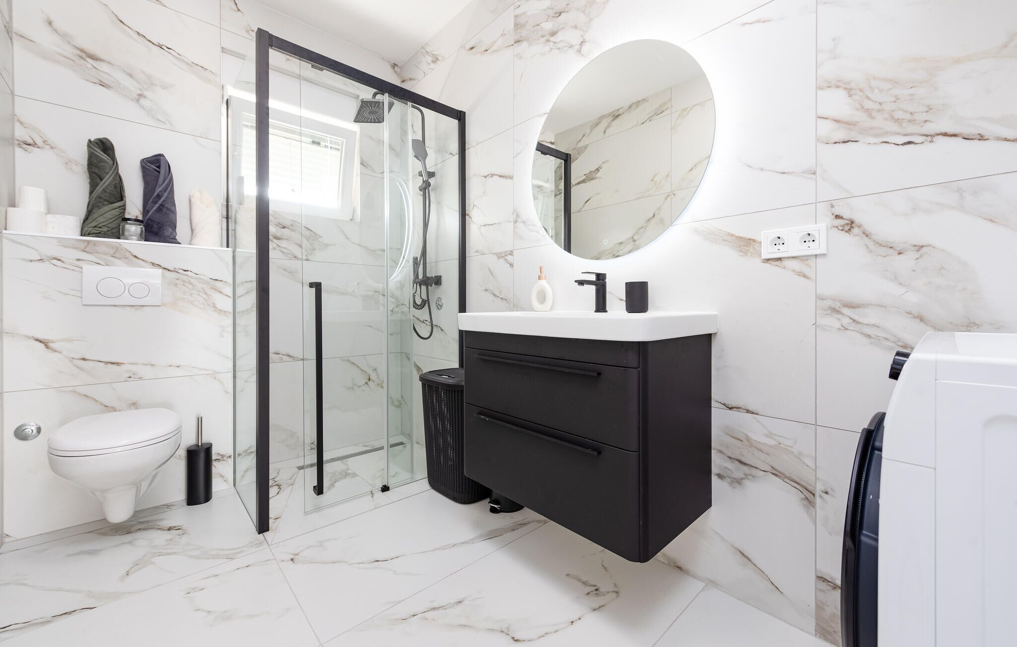 A modern bathroom with a glass-enclosed shower, a white toilet, a black vanity with a mirror, and marble flooring.