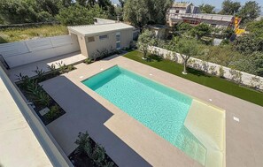 A rectangular swimming pool with clear water, surrounded by a low wall and a small building with a flat roof.