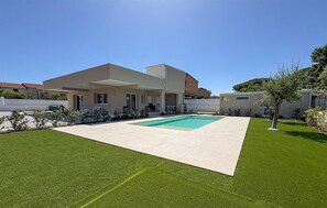 A modern two-story house with a swimming pool, a covered patio, and a well-maintained lawn.