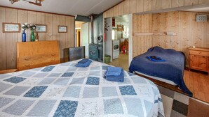 A bedroom with a large bed, wooden walls, a dresser, and a kitchenette in the background. - 1 bedroom gorgeous home in Ryssby (Ryssby)