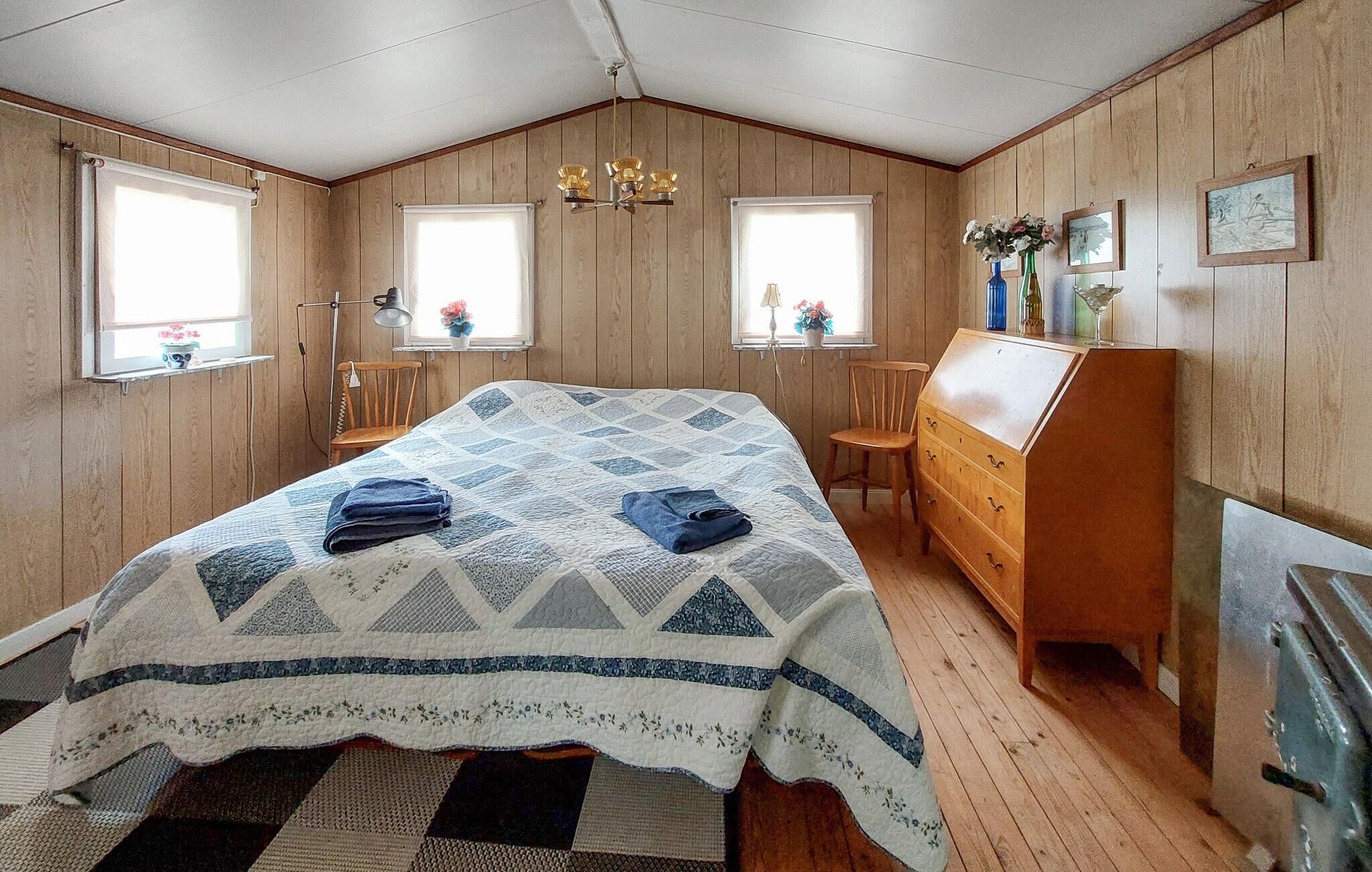 Une chambre à coucher comprenant un lit, une commode, deux chaises, un bureau et une fenêtre avec des rideaux.