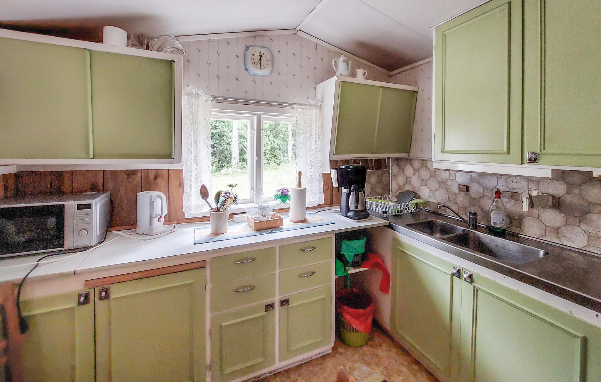 A kitchen with green cabinets, a microwave, a coffee maker, and a sink.