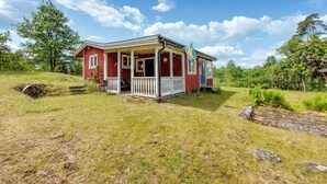 A red wooden house with a porch, surrounded by a grassy field and trees. - 1 bedroom gorgeous home in Ryssby (Ryssby)