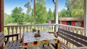 A covered patio with a table and benches, overlooking a green landscape and a red building. - 1 bedroom gorgeous home in Ryssby (Ryssby)