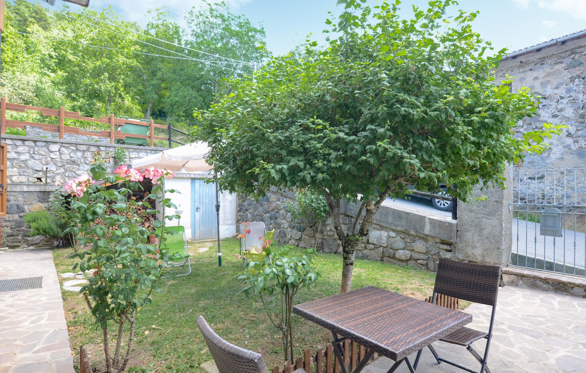 A patio with a table and chairs, surrounded by greenery and a stone wall.