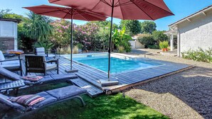 Ein Garten mit Swimmingpool, Liegestühlen und einem Pergola mit rotem Sonnenschirm.