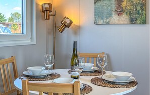 Une table à manger dressée avec des bols blancs, des verres à vin et une bouteille de vin, un tableau au mur et une lampe en arrière-plan.