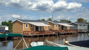 Een rij vakantiehuisjes met een steiger en boten, voor een bewolkte lucht.