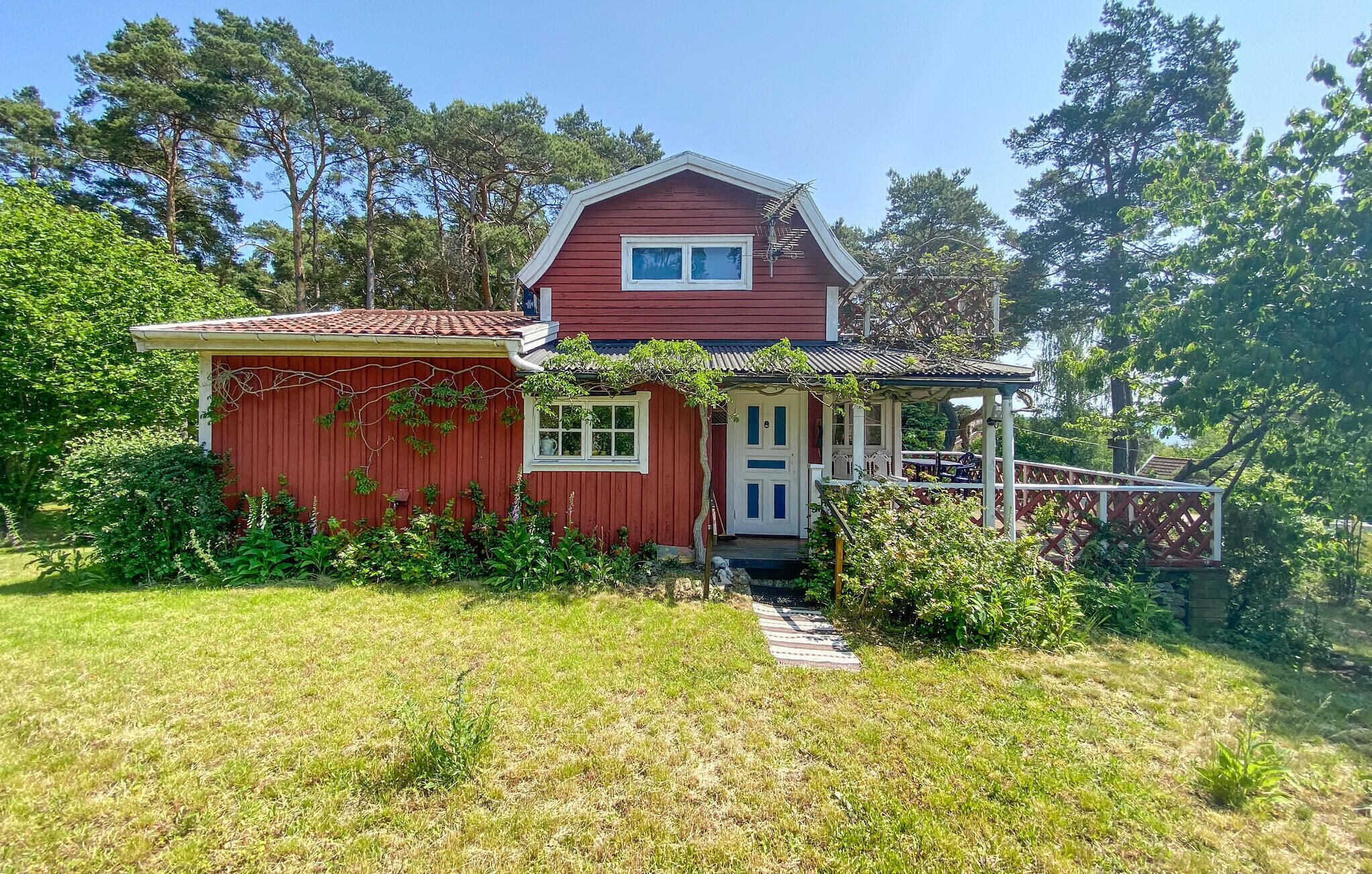 A red wooden house with a white door and windows, surrounded by greenery and trees.