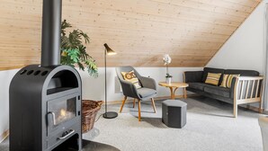 A cozy loft bedroom with a wood-burning stove, a gray armchair, a sofa, and a small round table. - Stunning home in Gråsten with sauna (Gråsten)