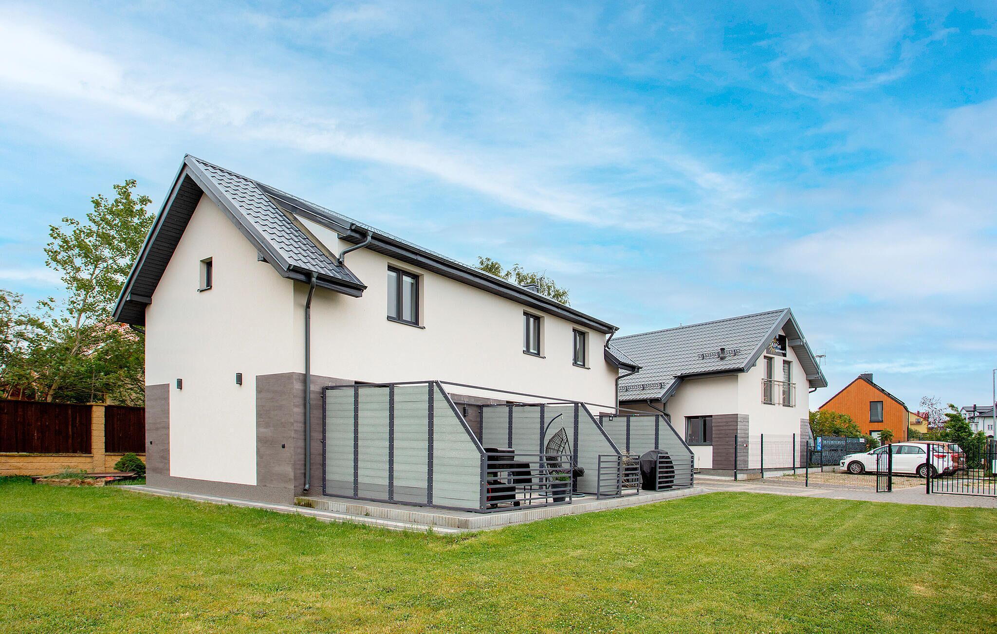 Een modern huis met twee verdiepingen, een schuin dak, een overdekt terras en een verzorgd gazon.