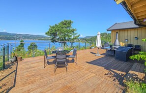 A wooden deck with a table and chairs, overlooking a lake with a view of distant hills. - Lovely home in Klokkarstua (Klokkarstua)