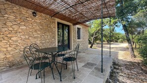 Un bâtiment en pierre doté d’un patio couvert, d’une table avec des chaises et d’une pergola.