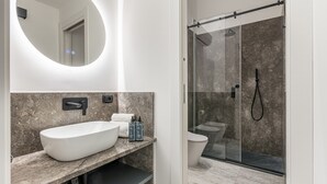 Un bagno moderno con un ampio lavabo ovale, una cabina doccia vetrata e uno specchio con illuminazione circolare.