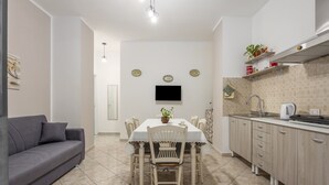 A compact living space with a dining table, chairs, a sofa, a kitchen area with cabinets and a sink, and a flat-screen TV mounted on the wall.