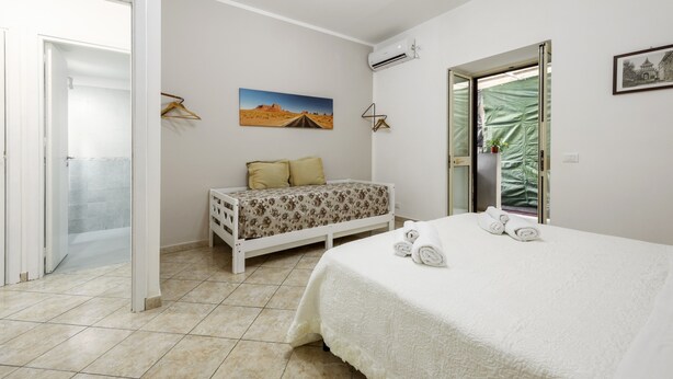 A bedroom with a bed, a sofa, a painting, an air conditioner, and a sliding door.