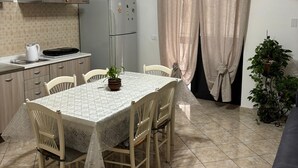 A kitchen with a dining table, chairs, a refrigerator, a stove, and a ceiling light fixture.